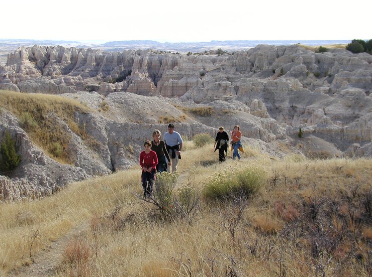 A group of hikers on a grassy trail backed by badlands geologic formations