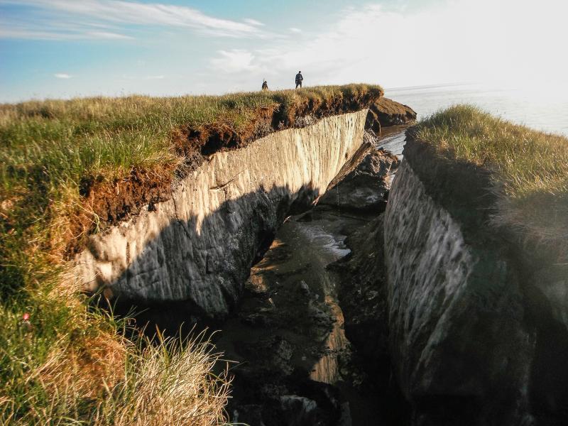 People standing on a cliff where a large block of frozen ground has broken off