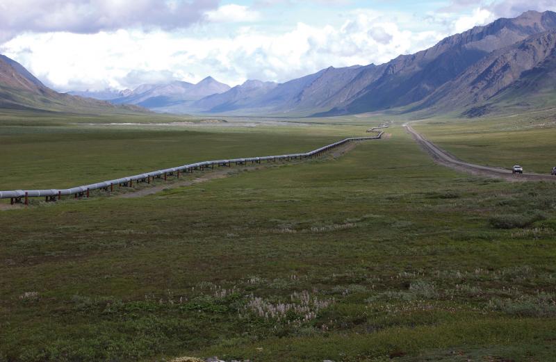 Sub-parallel pipeline and roadway cross a plain with mountains in the distance