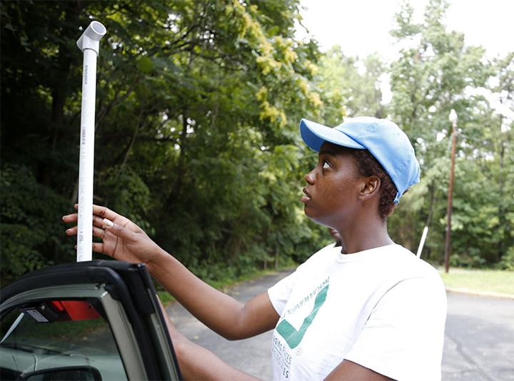 A youth volunteer from Groundwork RVA attaches a sensor unit onto a car.