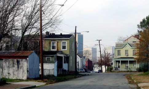 A street with wooden frame homes leading to city skyscrapers in the distance.